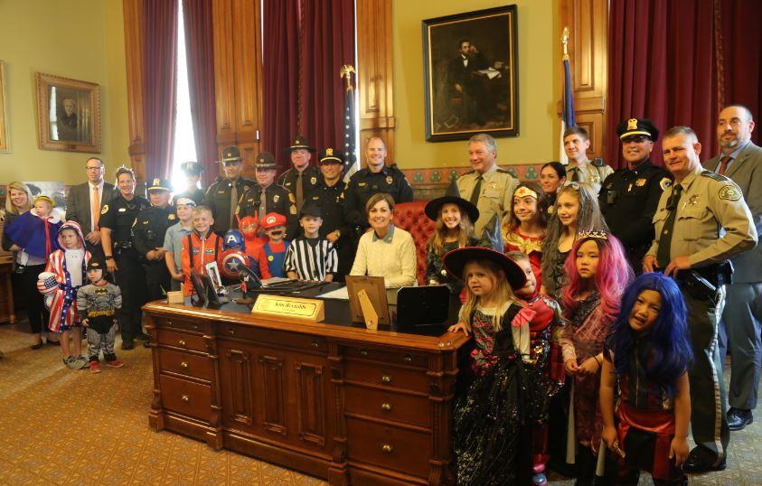 Photo of Governor Reynolds, kids in Halloween costumes, and multiple law enforcement officers from area agencies.